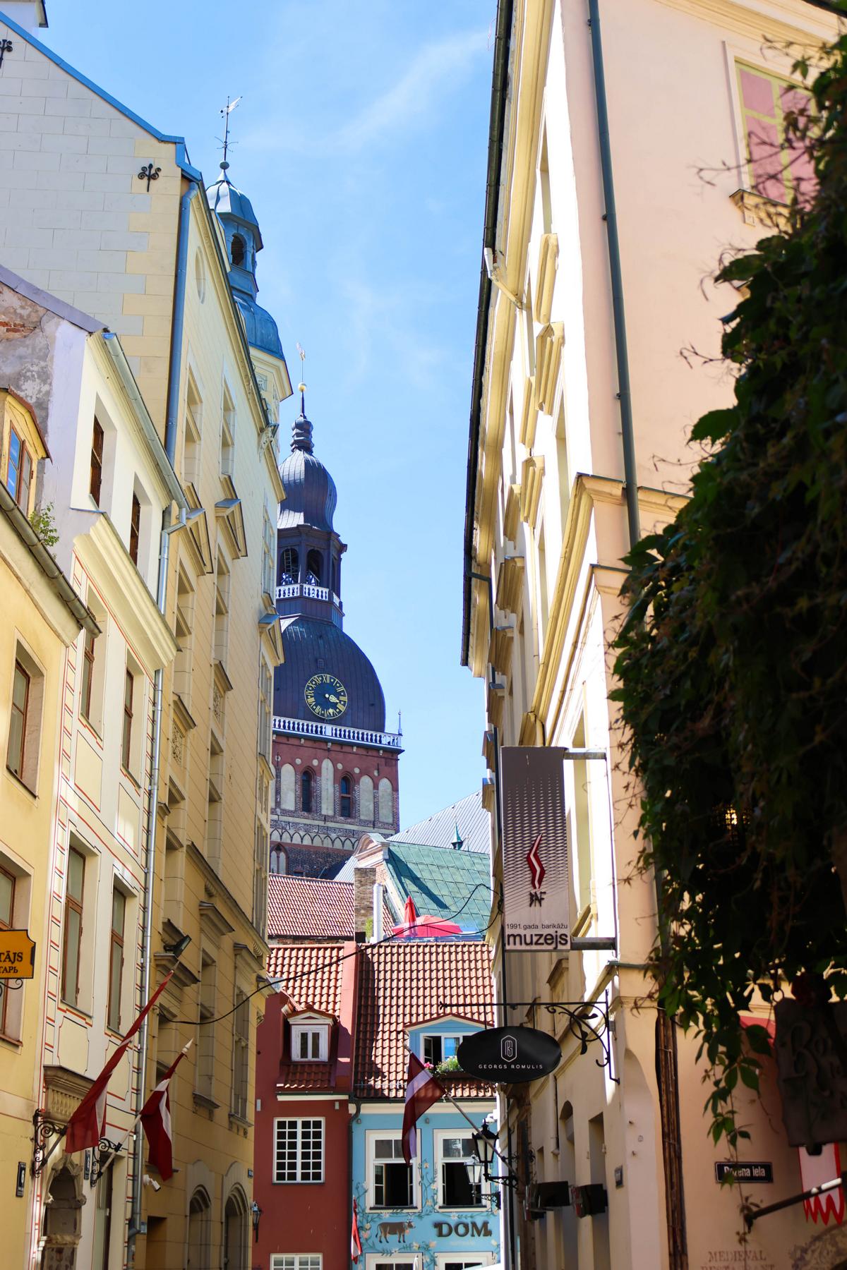 Blick durch eine schmale Gasse in der historischen Altstadt von Riga. Im Hintergrund ist der Turm der St.-Petri-Kirche zu sehen