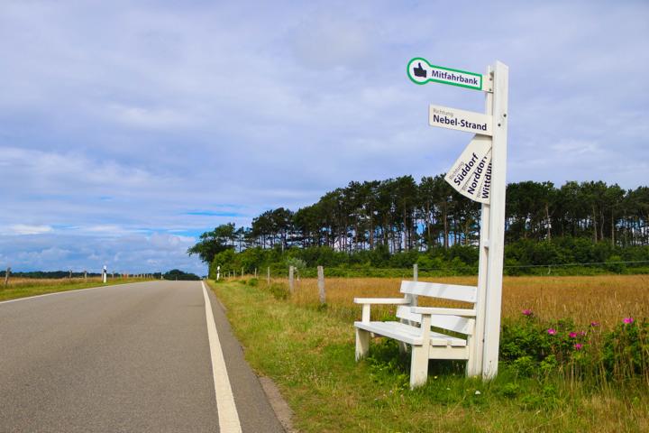 „Mitfahrerbank“ auf Amrum – Zielort aus den Klapptafeln auswählen, Platz nehmen, warten und mitgenommen werden – wer hier sitzt, fährt nicht nur mit, sondern wird Teil der Reise