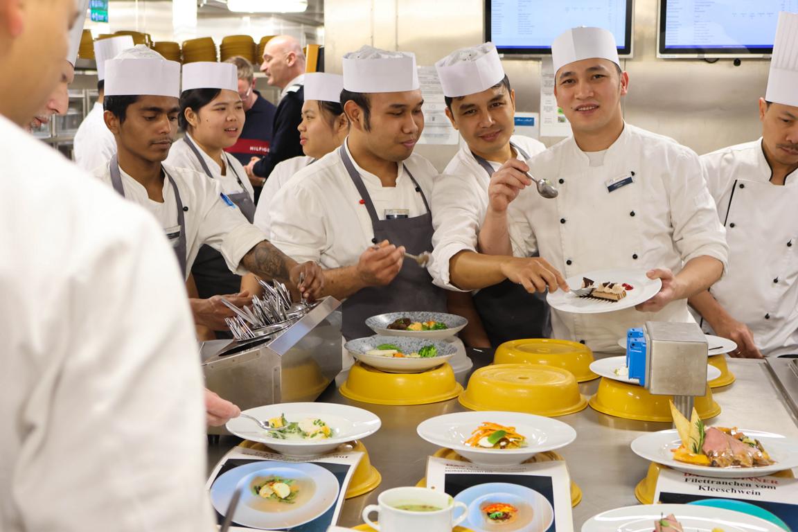 Gemeinsame Verkostung in der Galley: Die Küchencrew präsentiert ihre Gerichte und prüft sie vor dem Servieren auf Qualität und Geschmack