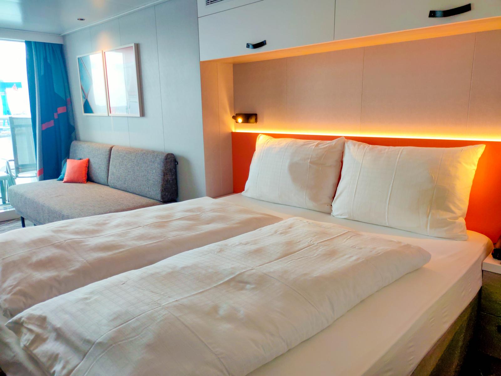 Blick in die Balkonkabine 10230 mit einer Wohnfläche von 17 m². Gemütliches Doppelbett im modernen Design. Die flexiblen schwarzen Leseleuchten verfügen über integrierte USB-C-Ladeanschlüsse