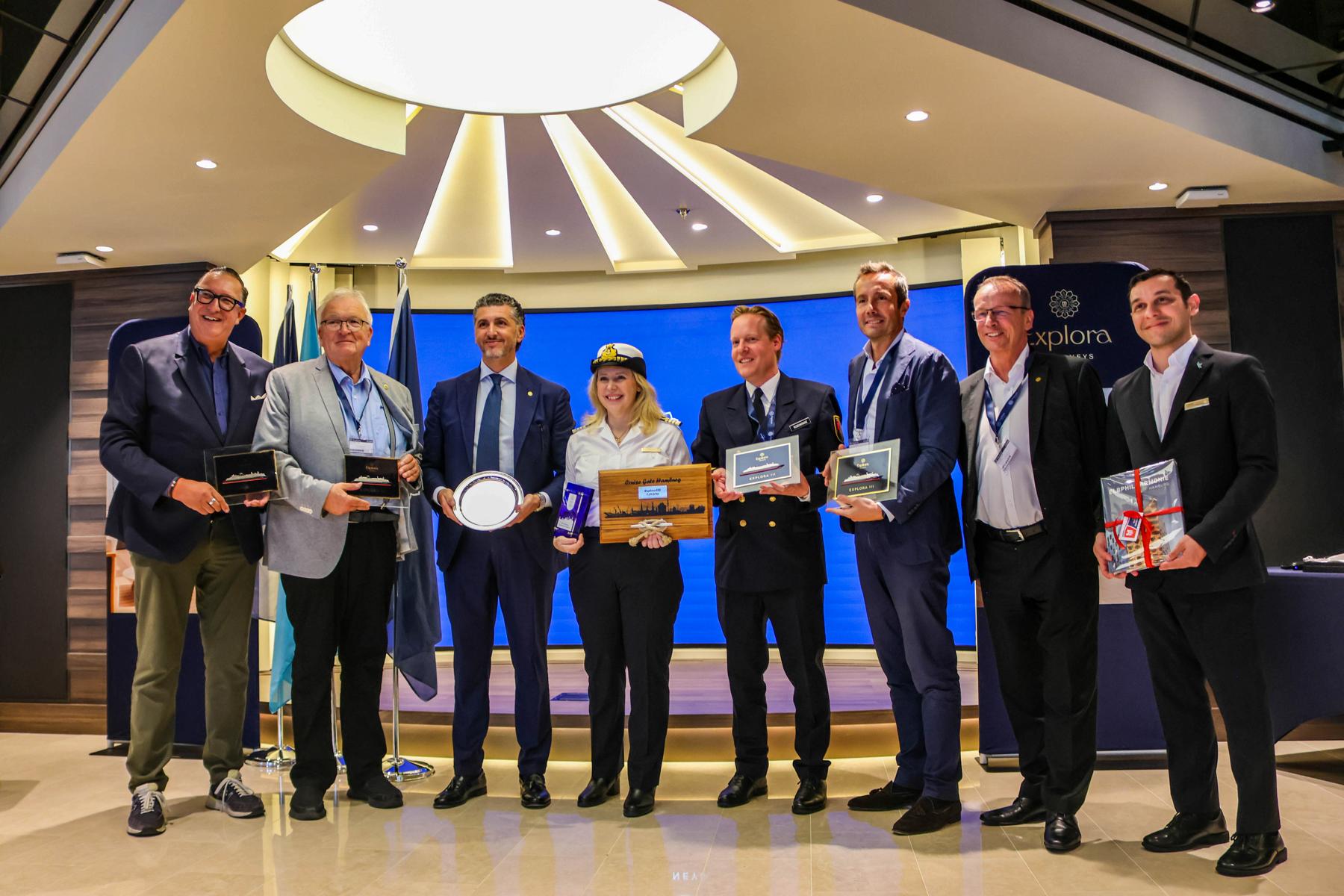 Die maritime Tradition des Plakettenaustausches. Im Foto v.l.n.r.: Alexander Napp (Managing Director PWL Port Services), Dr. Stefan Behn (Chairman Hamburg Cruise Net), Achille Staiano (Chief Commercial Officer Explora Journeys), Serena Melani (Kapitänin), Simon Rosenkranz (Harbour Master der Hamburg Port Authority), Simone Maraschi (Managing Director Cruise Gate Hamburg), Jörg Eichler (DACH-Geschäftsführer MSC Cruises und Explora Journeys), Host („EXPLORA III“)